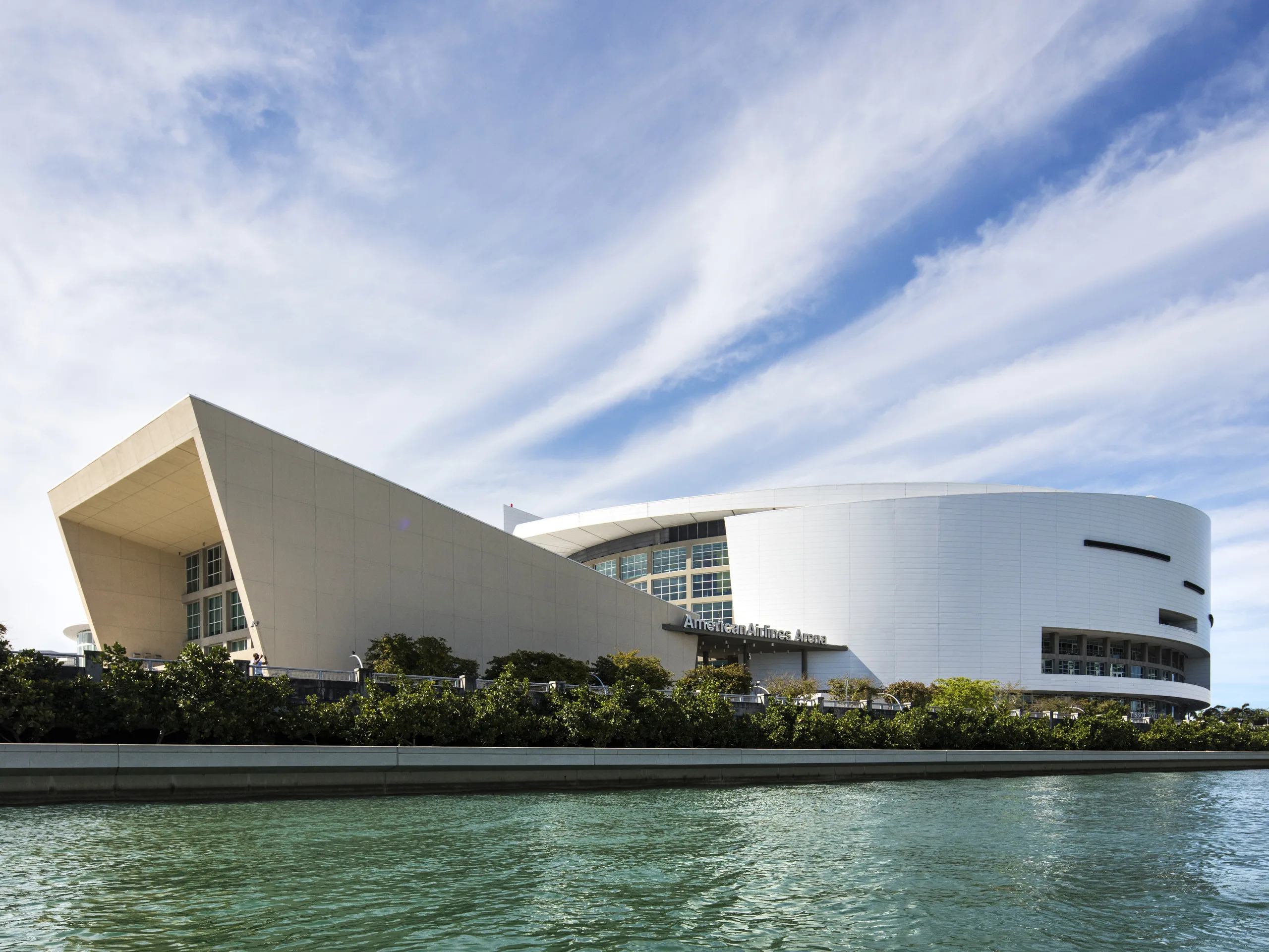 Modern white building with curved architecture near water, with blue sky and clouds above