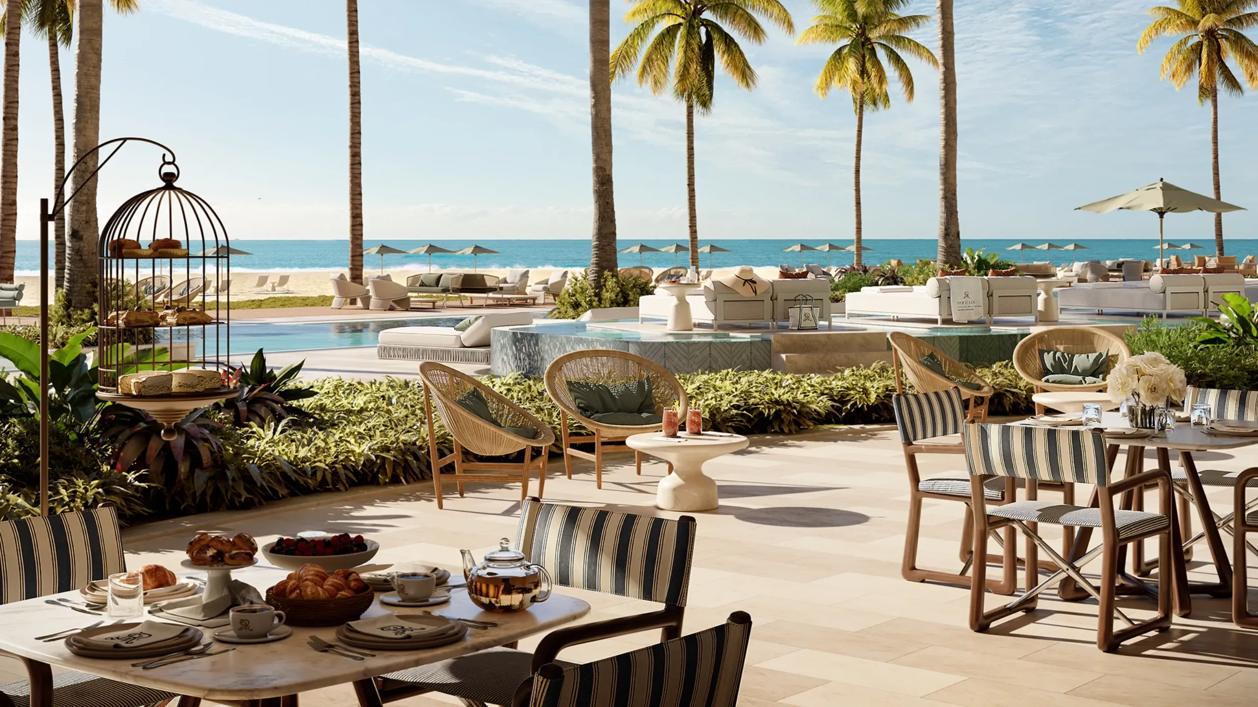 Outdoor dining area with a view of the pool, palm trees, and the ocean in the background.