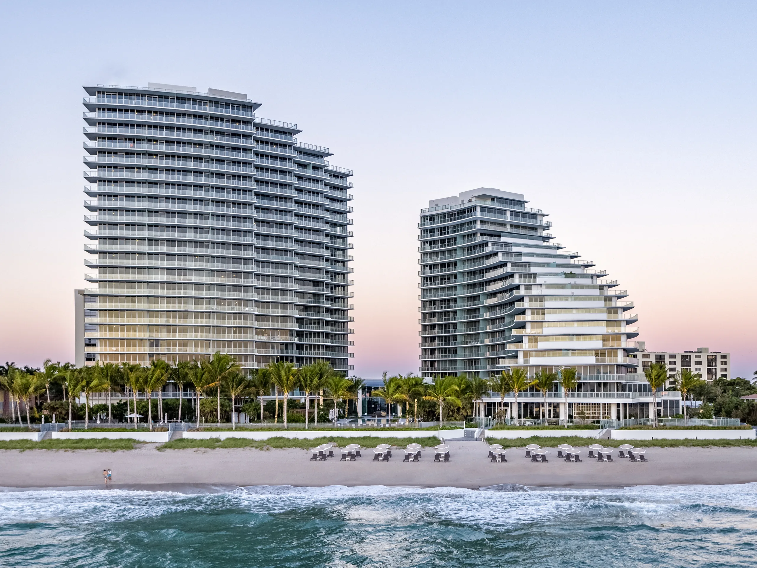 Two modern high-rise buildings with glass facades along the beach at sunset