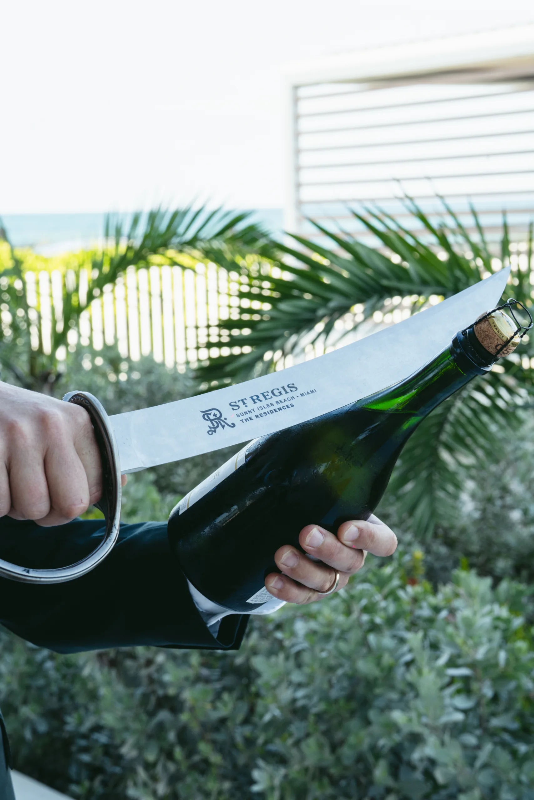 Person holding a champagne bottle wrapped in a St. Regis paper with a tropical background