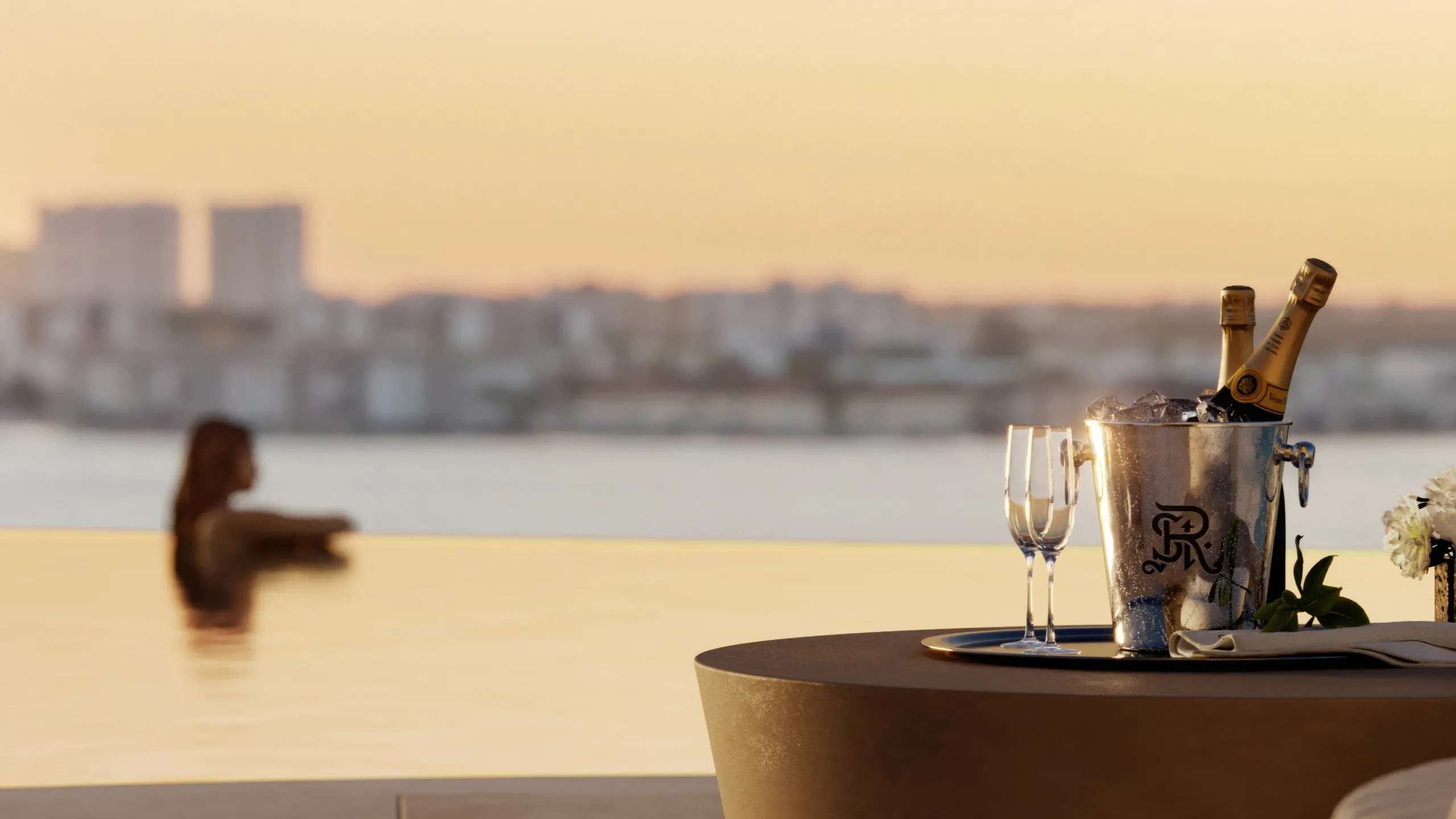 Champagne bottles in an ice bucket with two glasses and flowers on a table at sunset